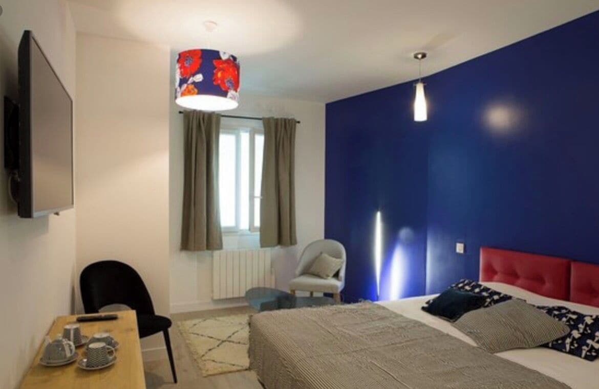 Une chambre à coucher avec un lit, une chaise, une table, un téléviseur et une fenêtre avec des rideaux.