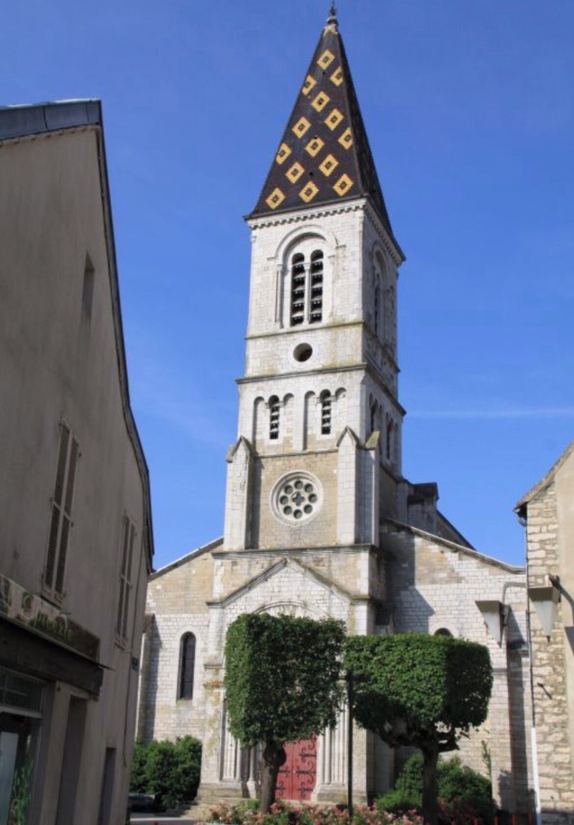 Eine Kirche mit einem hohen Glockenturm, Rundbogenfenstern und einem kreisförmigen Fenster an der Fassade.