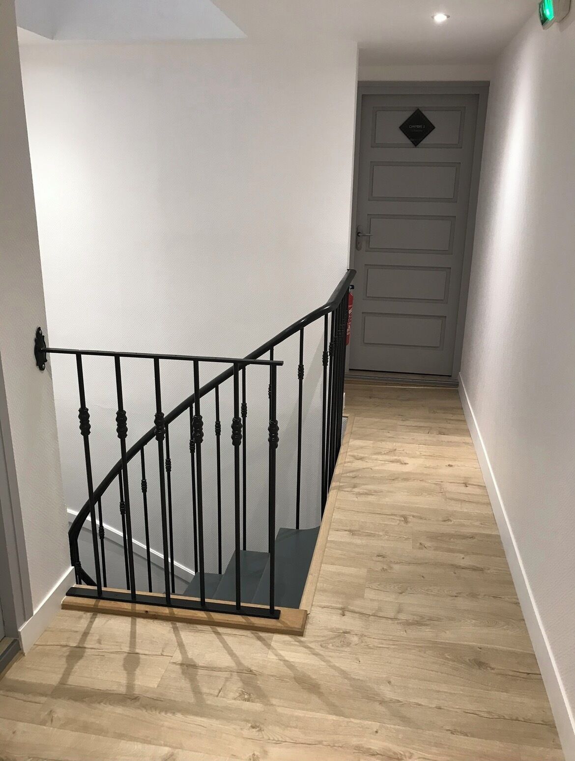 Un escalier avec une rampe en métal noir, un plancher en bois et un mur blanc.