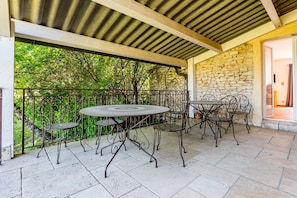 Une terrasse extérieure avec un mur en pierre, une rambarde en métal et une table entourée de chaises.
