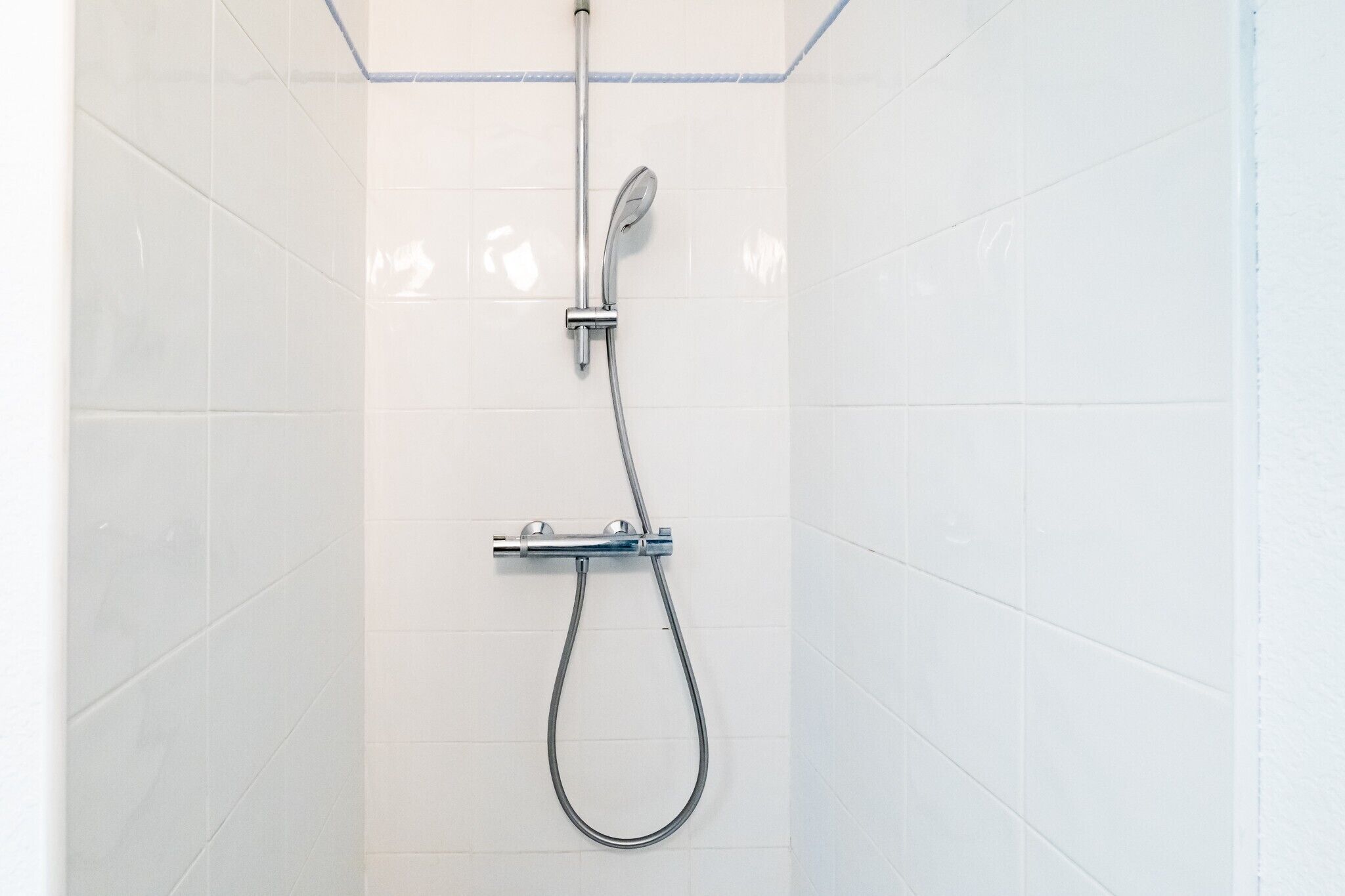 Ducha con cabezal de ducha de mano y cabezal de ducha fijo, montada en una pared de azulejos blancos.