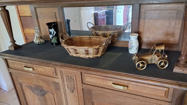 Une commode en bois avec des tiroirs, un miroir et des objets décoratifs, notamment un panier en osier, une petite voiture jouet et un vase.