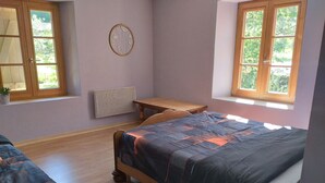 Une chambre à coucher comprenant un lit, une petite table, un radiateur et une fenêtre donnant sur un paysage verdoyant.