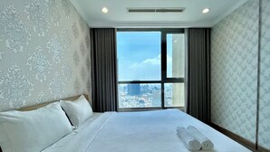 Hotellihuone, jossa on suuri sänky, ikkunasta avautuva näkymä kaupungin ylle ja kuviollinen seinä.