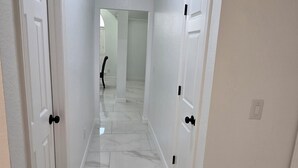 A hallway with white doors, a ceiling vent, and a marble floor. - Adorable 2-bedroom house with AC in charming Lewisville (Lewisville)
