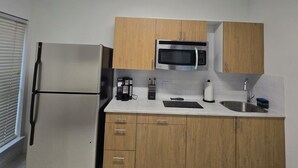 A modern kitchen with a stainless steel refrigerator, wooden cabinets, a microwave, and a sink. - Adorable 2-bedroom house with AC in charming Lewisville (Lewisville)