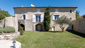 A stone building with a central archway, a small tree, and a stone wall. - Holiday Home “Bastide de Marius” with Shared Pool, Terrace, and Wi-Fi (Redortiers)