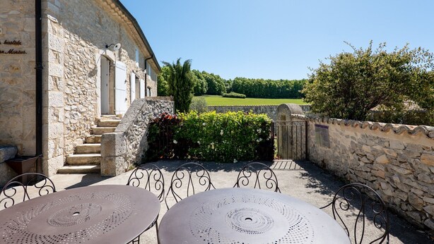 A stone building with a staircase, outdoor seating area with metal tables and chairs, and a view of a green field. - Holiday Home “Bastide de Marius” with Shared Pool, Terrace, and Wi-Fi (Redortiers)