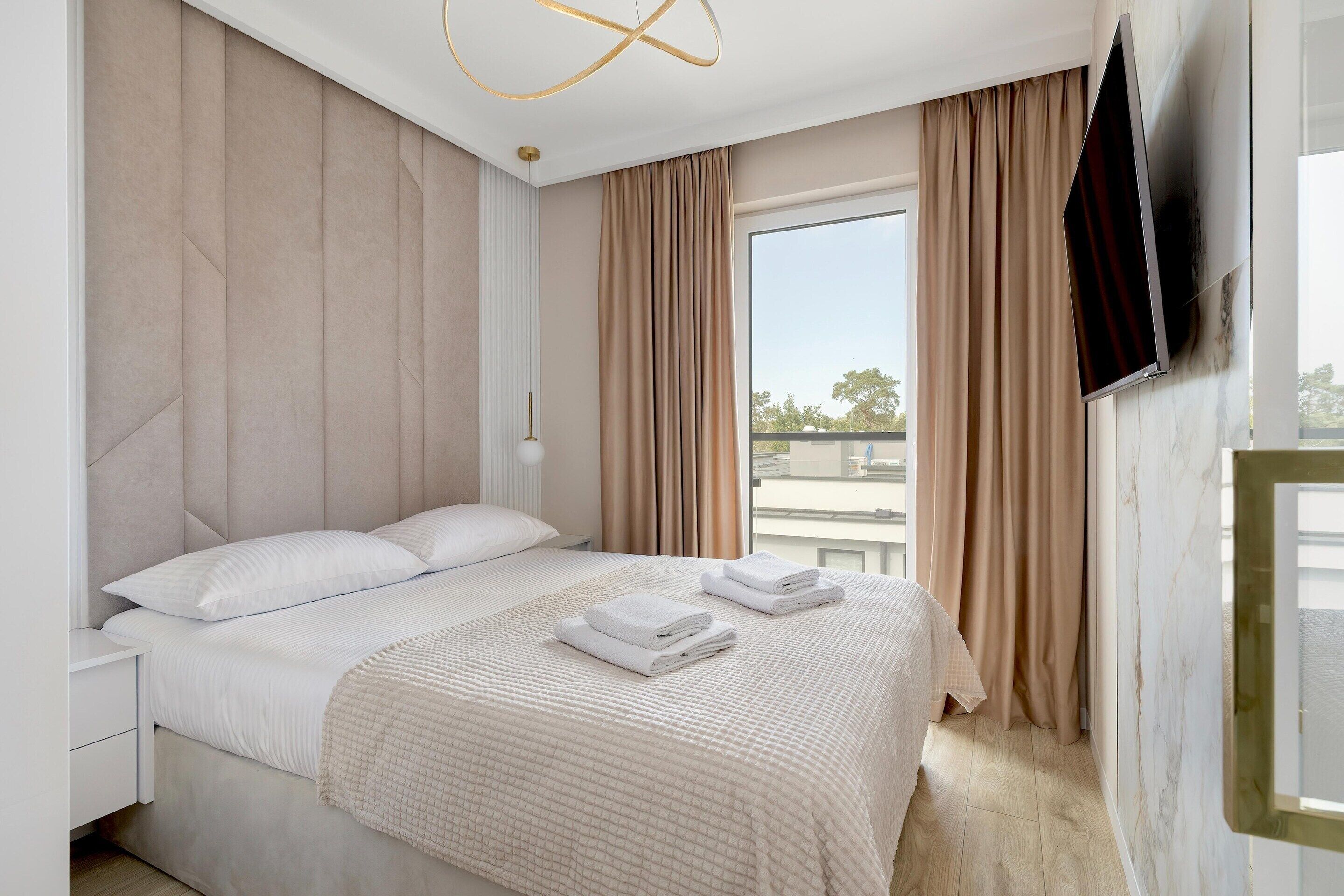 Ein Hotelzimmer mit einem Bett, einem an der Wand montierten Fernseher und einem Fenster mit Vorhängen.