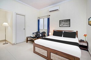 A hotel room with a bed, a desk, a chair, a lamp, a picture on the wall, and an air conditioning unit. - Deluxe Hebbal Mysore Green Orchid Resort (Mysore)