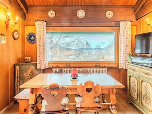 Comedor de madera con un ventanal grande, un radiador debajo y un televisor sobre un mueble.