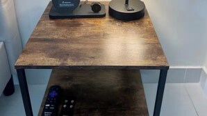Un comodino in legno con una lampada, un telecomando e un piccolo dispositivo nero.