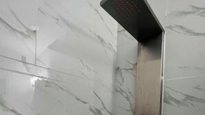 Una doccia con soffione quadrato, un pannello di controllo e una parete rivestita di piastrelle effetto marmo.