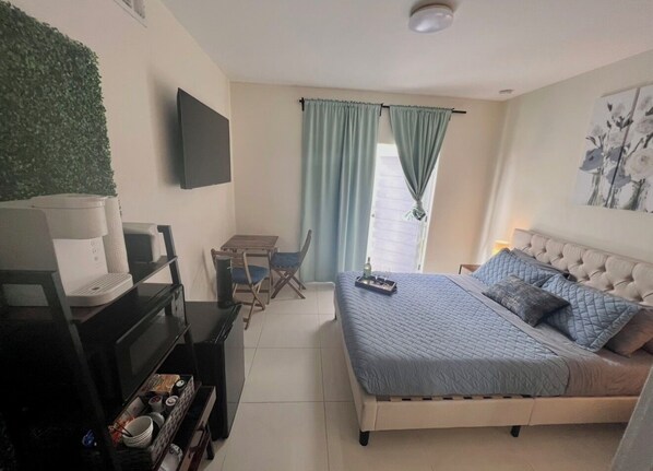 Une chambre à coucher comprenant un lit, un bureau, une chaise, un téléviseur à écran plat et une fenêtre avec des rideaux.