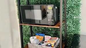 Cucina con un forno a microonde su uno scaffale, un cestino della spazzatura e una parete verde.