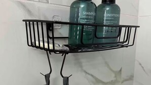 Un bagno con una parete in marmo, uno scaffale in metallo nero che contiene due bottiglie di shampoo e balsamo, e un paio di pantofole grigie appese allo scaffale.
