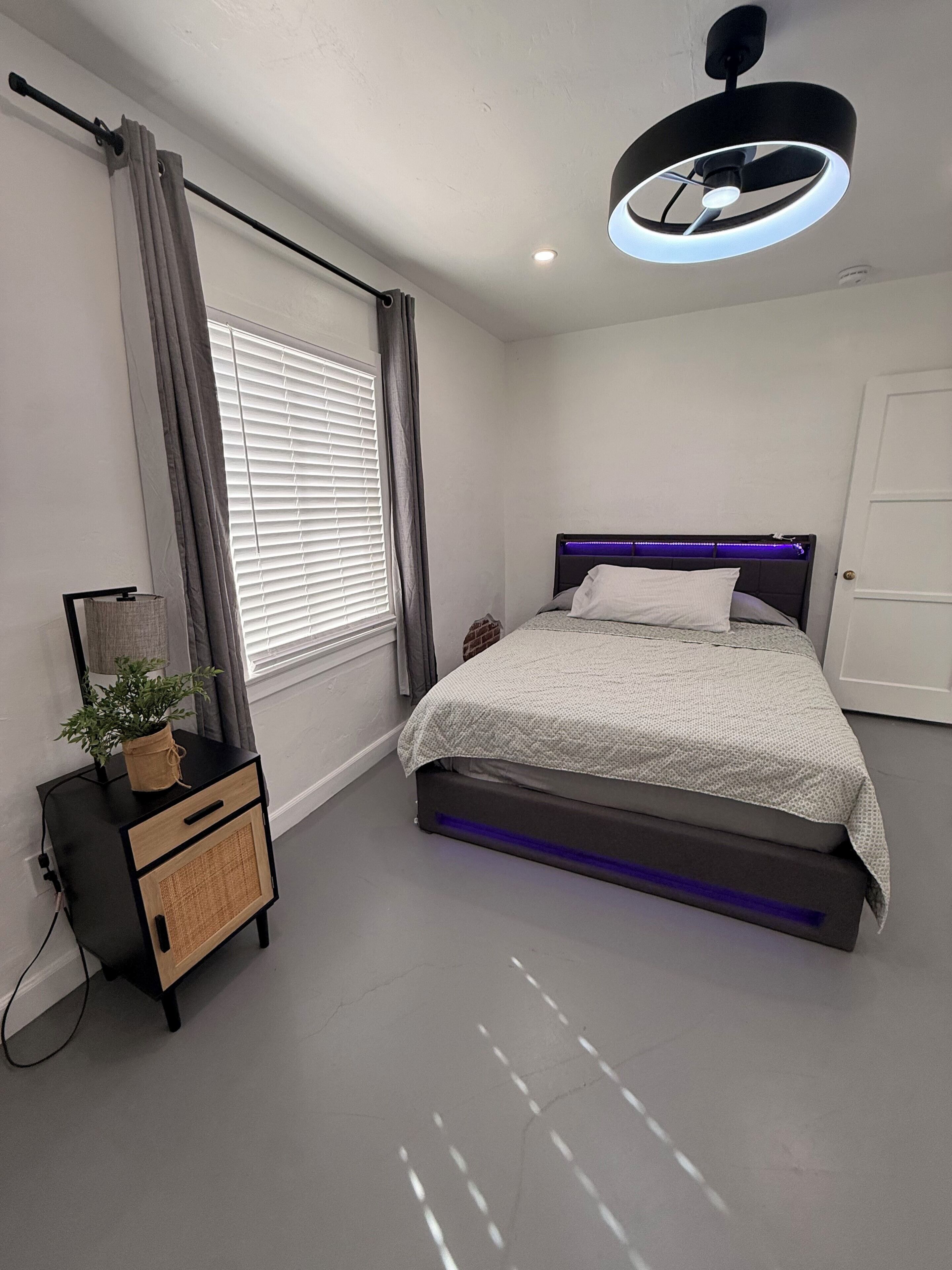 A modern bedroom with a bed, bedside table, curtains, and a ceiling light fixture.