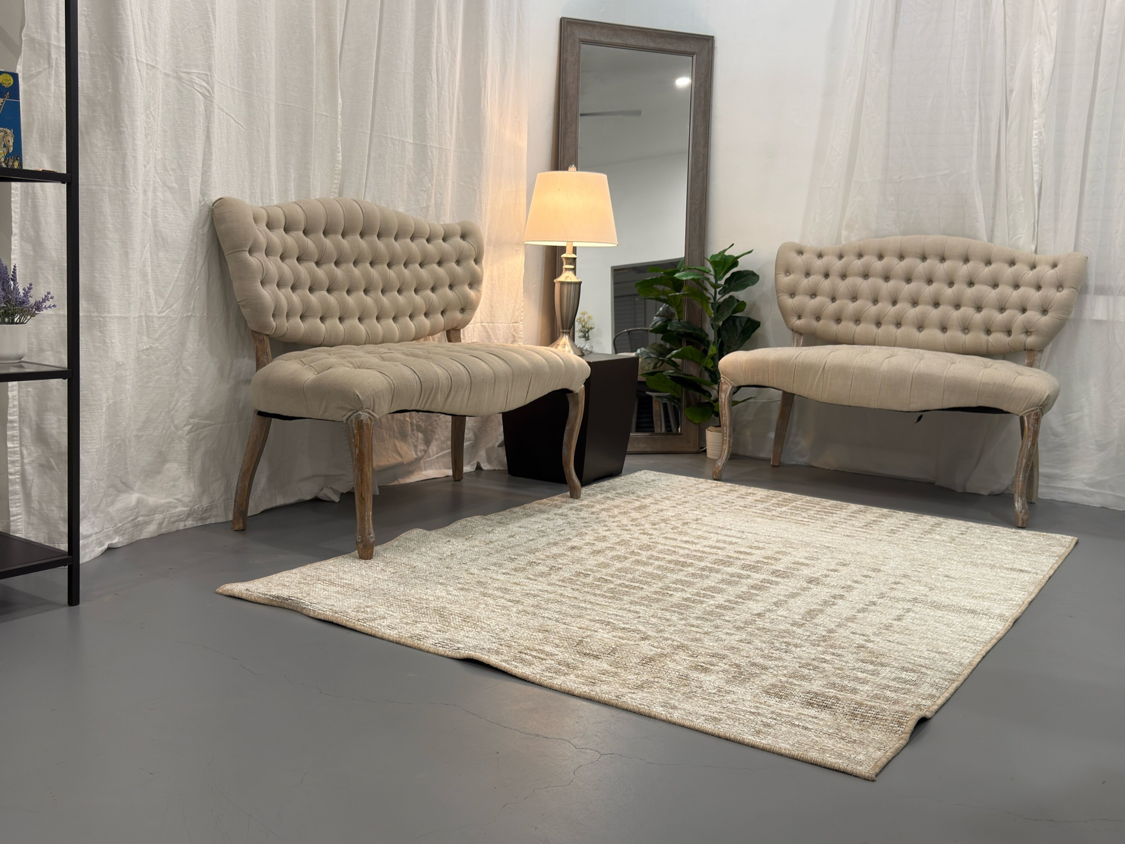 Una habitación con dos sillones color beige, una mesita, una lámpara, un espejo y una alfombra texturizada sobre un suelo gris.