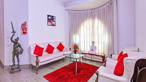 A living room with a white sofa, red cushions, a glass coffee table, a statue, and a Buddha statue. - Suite Vijaya Residency (Visakhapatnam)
