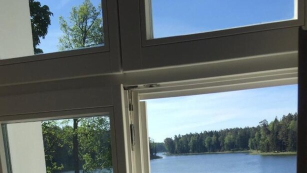 A view through a window with a wooden swan decoration, a lake, and a dock. - Comfortable House With Access to the Lake, Masuria (Ruciane-Nida)