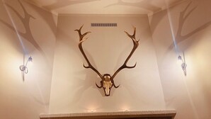 A room with a stone fireplace, a mounted deer skull, and a table with a candle and glasses. - Comfortable House With Access to the Lake, Masuria (Ruciane-Nida)