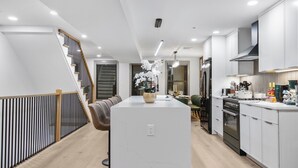 A modern kitchen with white cabinets, a central island, and a staircase on the left. - North End 2-Story Penthouse / Prime Location (Boston)