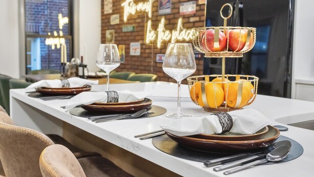 A dining area with a long table set for two, featuring plates, cutlery, and a fruit basket. - North End 2-Story Penthouse / Prime Location (Boston)