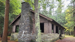 A rustic cabin with a stone chimney, wooden walls, and a porch.