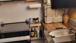 A kitchen with a microwave, oven, and a stone wall. There are shelves with kitchen utensils and bottles.