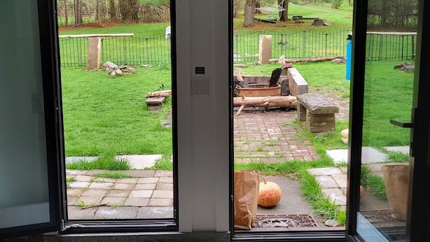 A room with a door leading to a backyard with a welcome mat, a stone bench, and a small pumpkin.