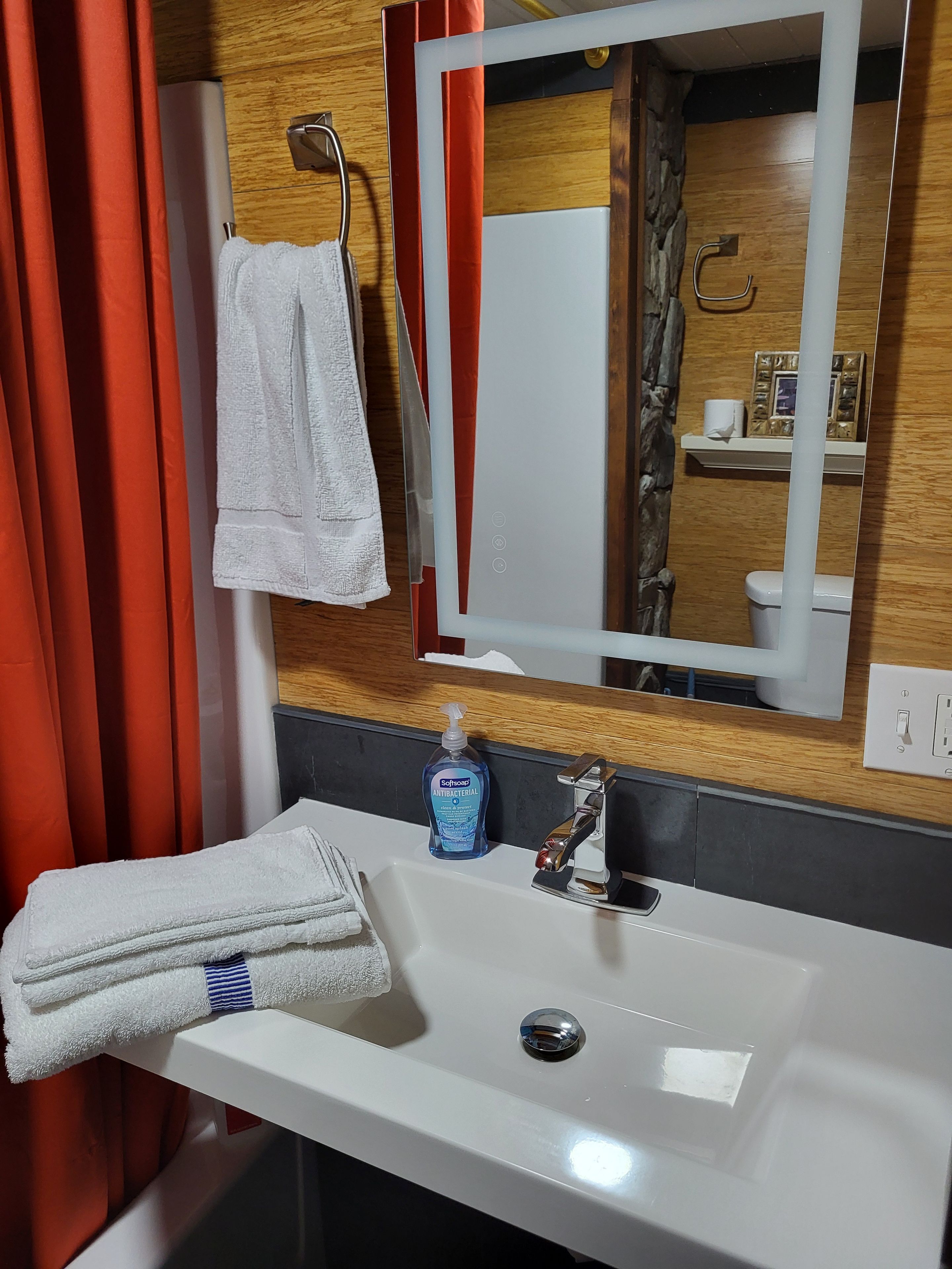 Une salle de bain avec un lavabo blanc, un miroir, un porte-serviettes et un flacon de savon pour les mains.