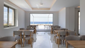 A modern dining area with a view of the beach, featuring wooden tables and chairs, large windows, and a clean, minimalist design. - Falasarna Bay Hotel (Kissamos)