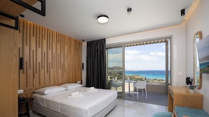 A modern hotel room with a bed, a desk, a chair, a balcony with a view of the sea, and a large window. - Falasarna Bay Hotel (Kissamos)