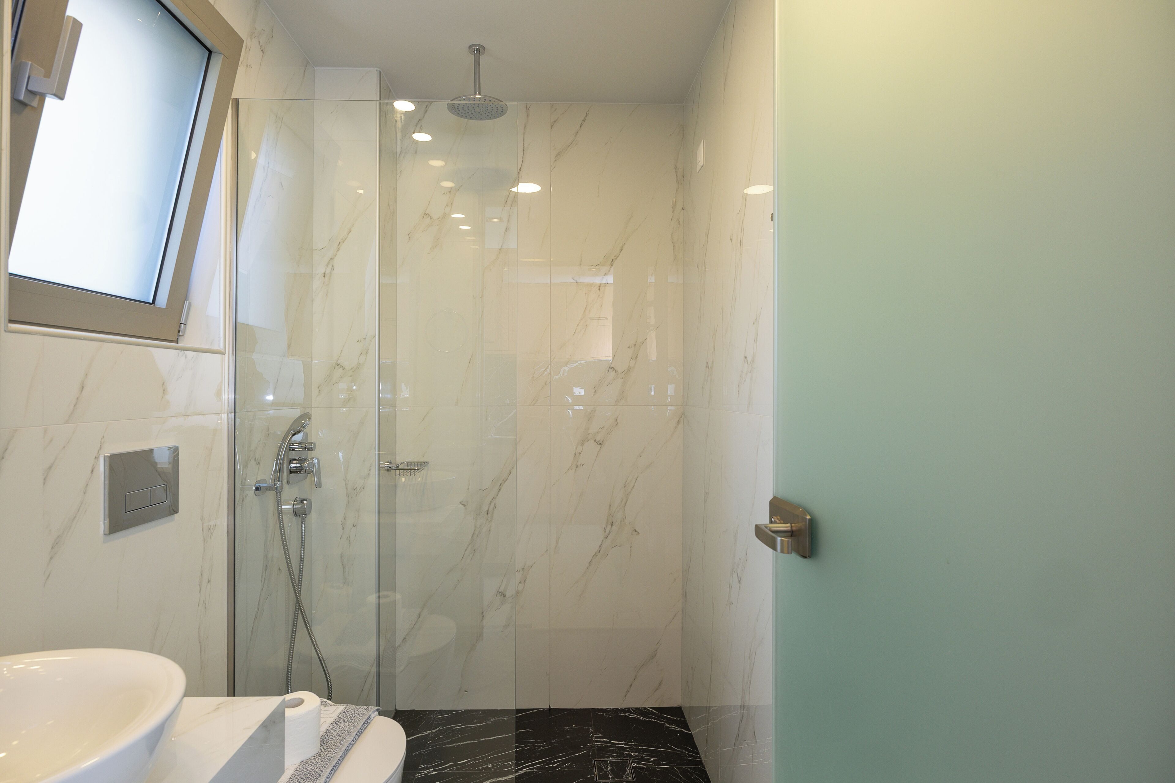 A modern bathroom with a glass-enclosed shower, a sink, and a toilet.