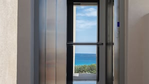 An elevator with a glass door leading to a balcony with a view of the sea. - Falasarna Bay Hotel (Kissamos)