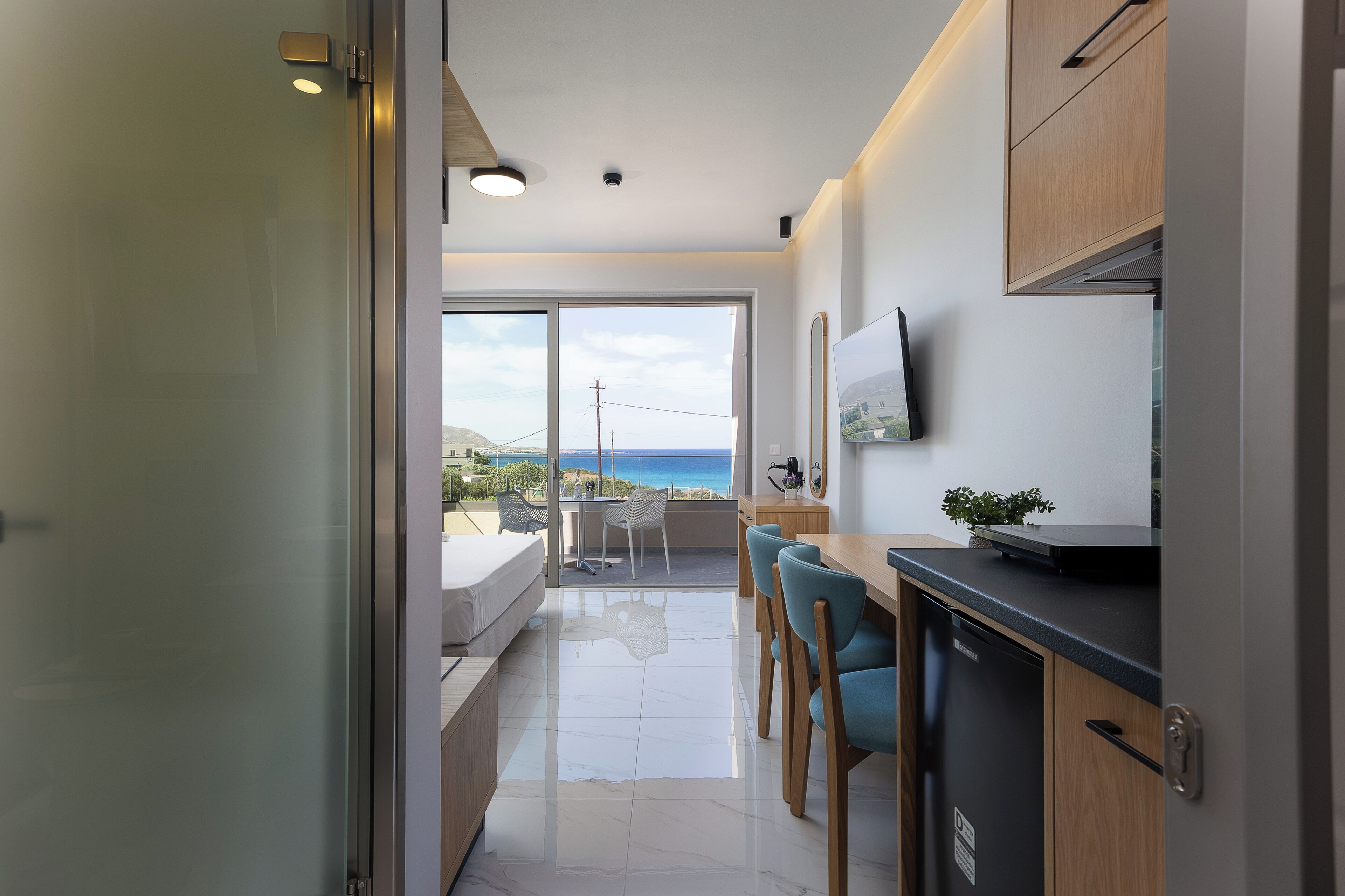 A modern kitchen with a dining area, a large window with a view, and a flat-screen TV mounted on the wall.