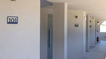 A corridor with numbered doors, a fire extinguisher, and a light fixture on the wall.