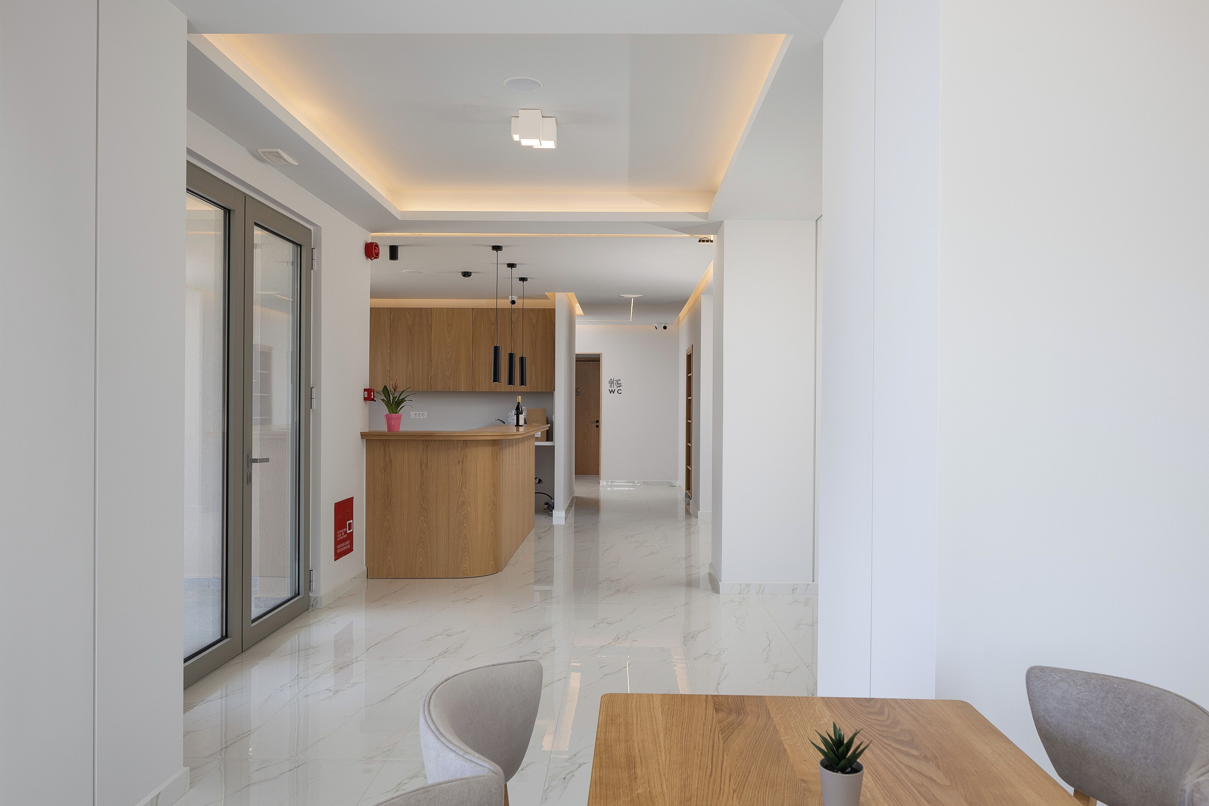 Una moderna hall d'albergo con una reception, un bancone in legno e un'area relax con tavolo e sedie.