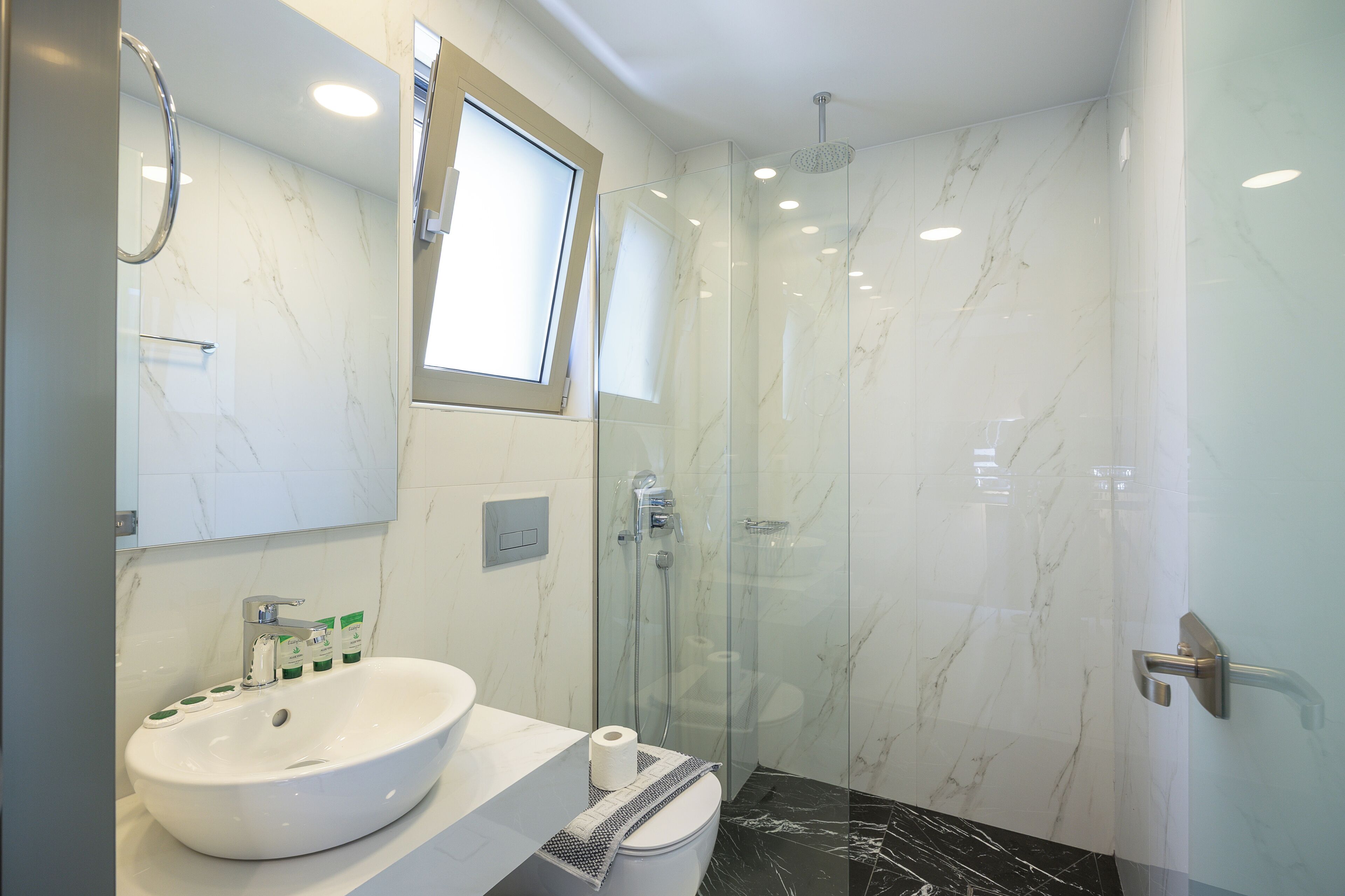 A modern bathroom with a white sink, glass shower enclosure, and marble walls.