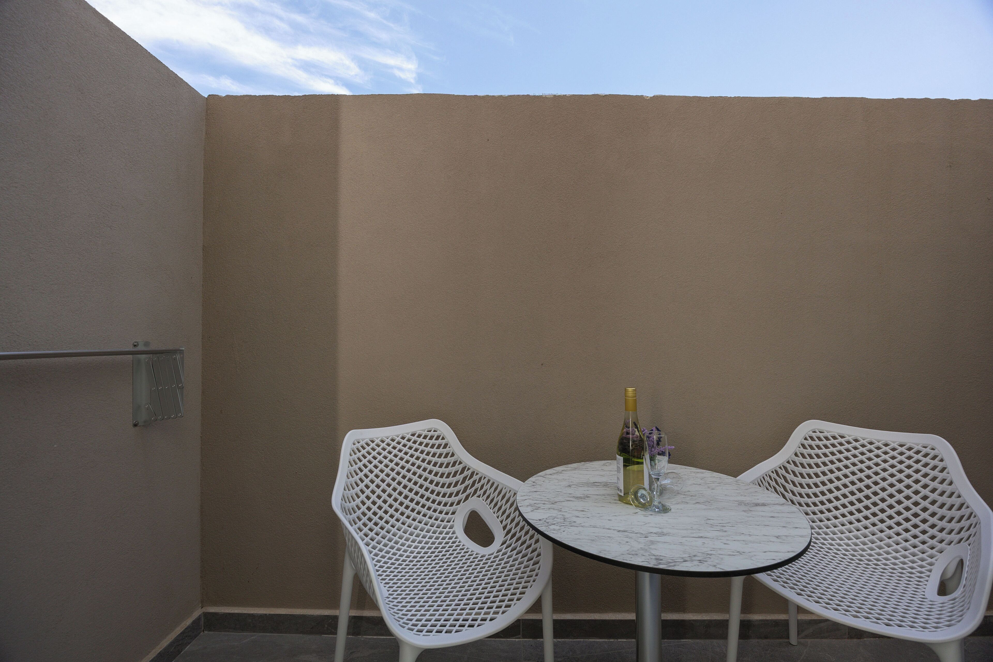 A small outdoor seating area with a round table and two white chairs, a bottle of wine, and a glass on the table.