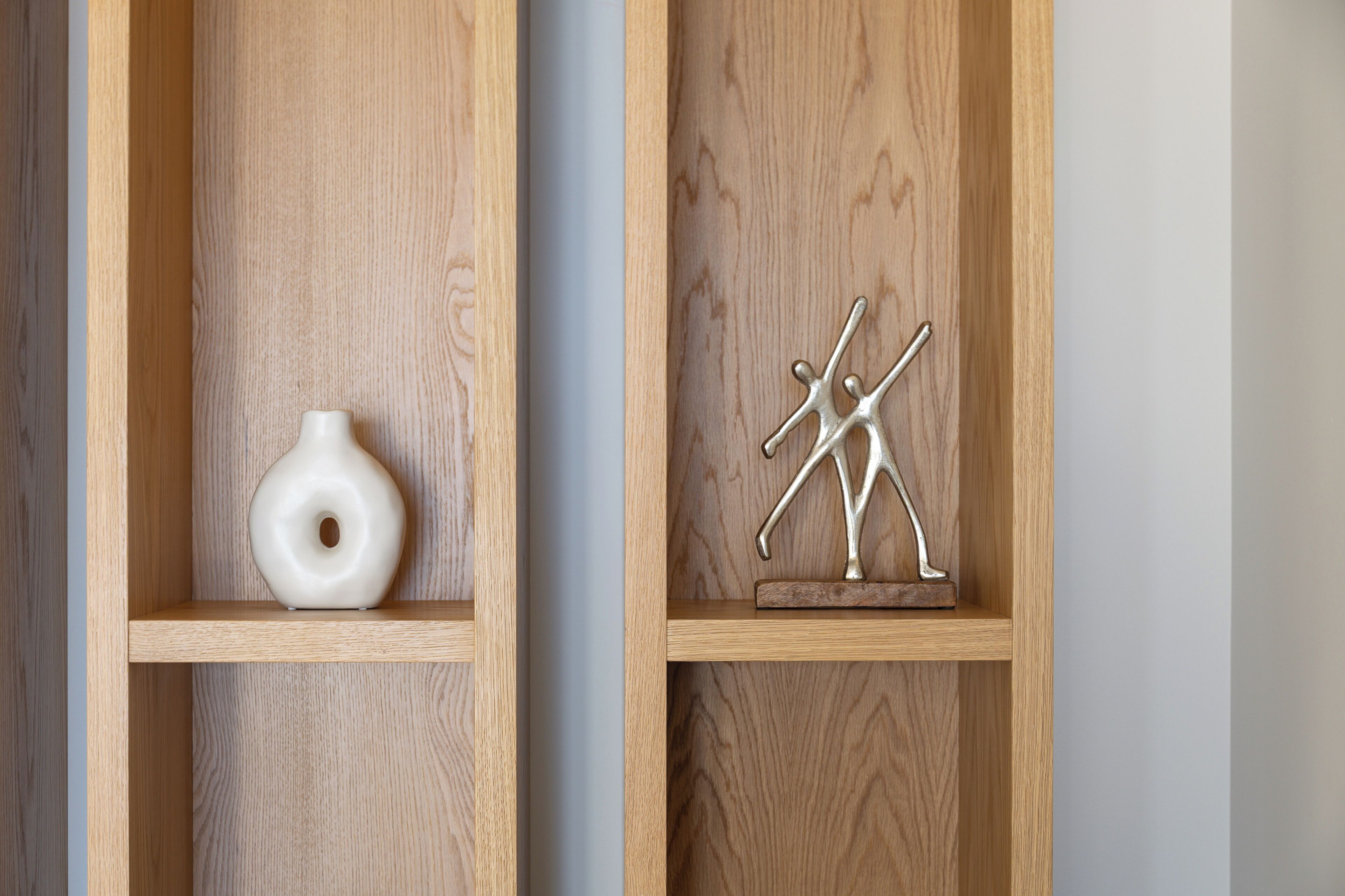 Two wooden shelves with a white vase and a metal sculpture.