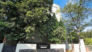 Placa com a inscrição 'TOWNHOUSE', com parede de pedra e portão, cercada por árvores.