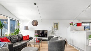 A modern living room with a sofa, armchair, and coffee table, a TV, and a kitchen area with cabinets and a countertop. - "Sofus" - 800m from the sea by Interhome (Væggerløse)