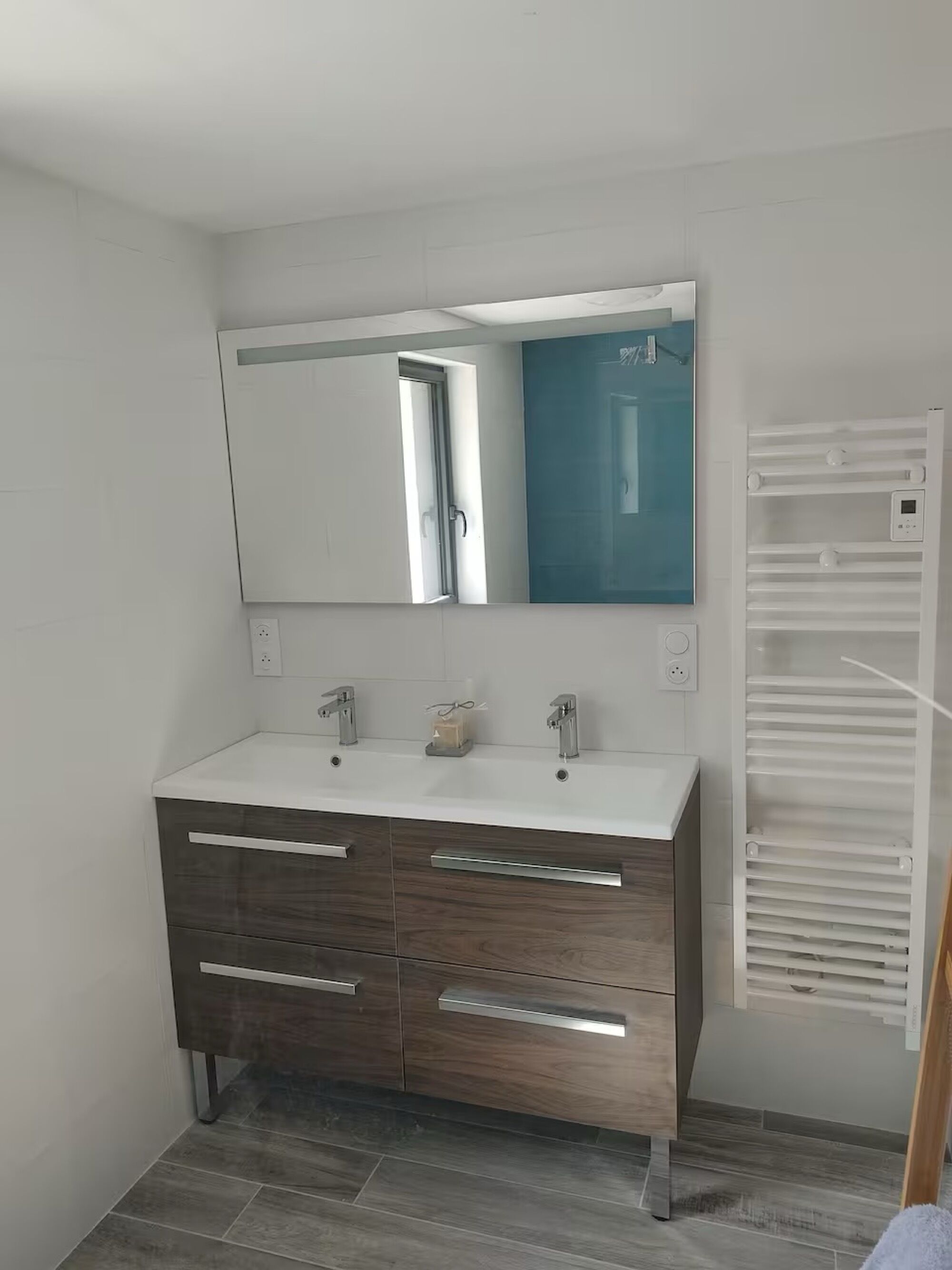 Une salle de bain moderne avec un meuble-lavabo blanc, deux vasques, un grand miroir et un porte-serviettes intégré.