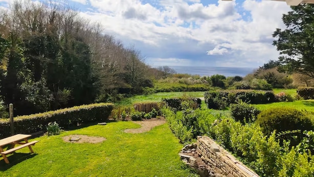 Un jardín bien cuidado con una mesa de picnic, un muro de piedra y vistas al mar.