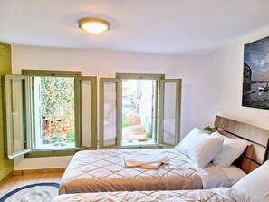A bedroom with a bed, a window with a view of a garden, and a painting on the wall. - Icarus Loft with rooftop terrace in old town (Chania)