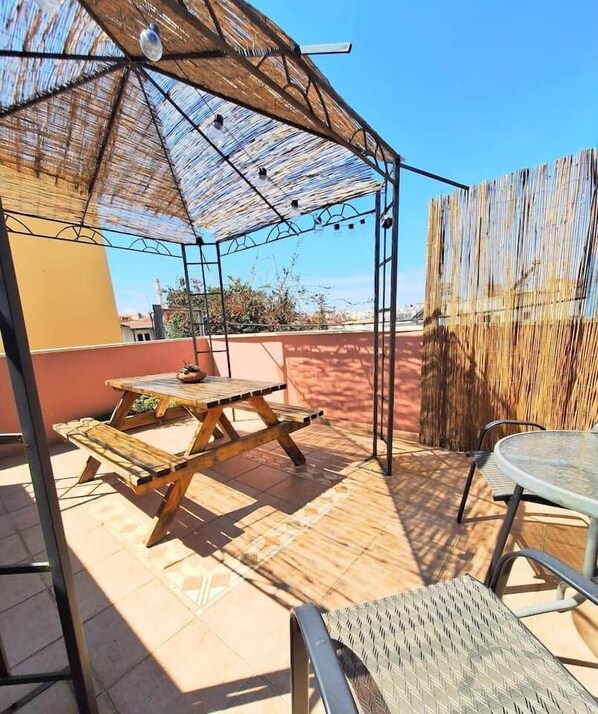 An outdoor patio with a wooden table and chairs, a metal umbrella, and a bamboo fence. - Icarus Loft with rooftop terrace in old town (Chania)