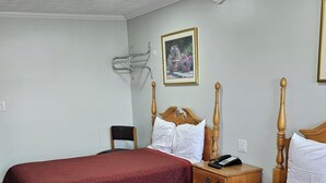 A hotel room with two beds, a wooden headboard, a small bedside table with a phone, a wall-mounted air conditioning unit, and a framed picture on the wall. - Deluxe Inn Elkton (Elkton)