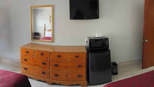 A room with a wooden dresser, a black refrigerator, a television on the wall, a mirror, and a door. - Deluxe Inn Elkton (Elkton)