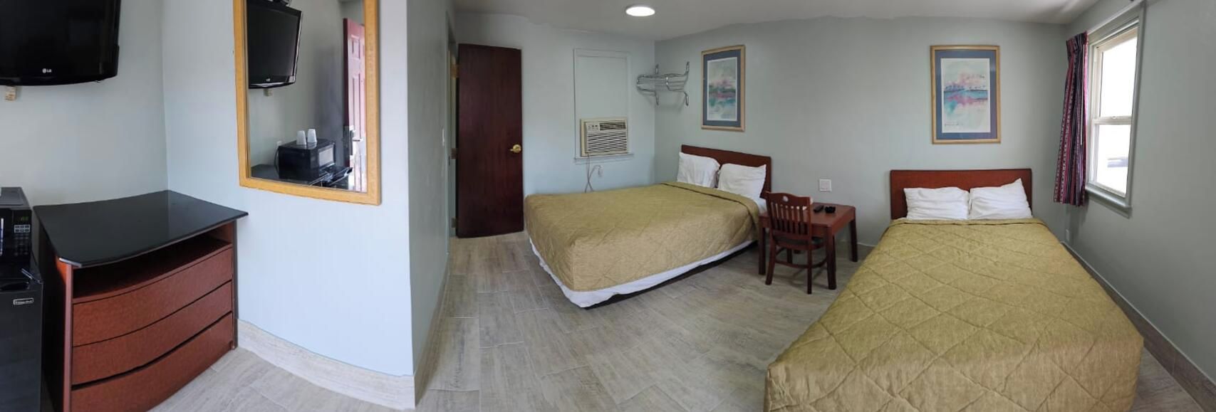 Ein Hotelzimmer mit zwei Betten, einem Schreibtisch, einem Stuhl, einem Fernseher und einem Kleiderschrank.